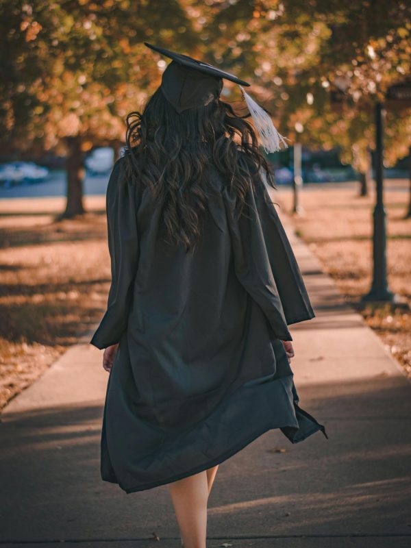 Back view of a graduate walking in an autumn park in academic dress.